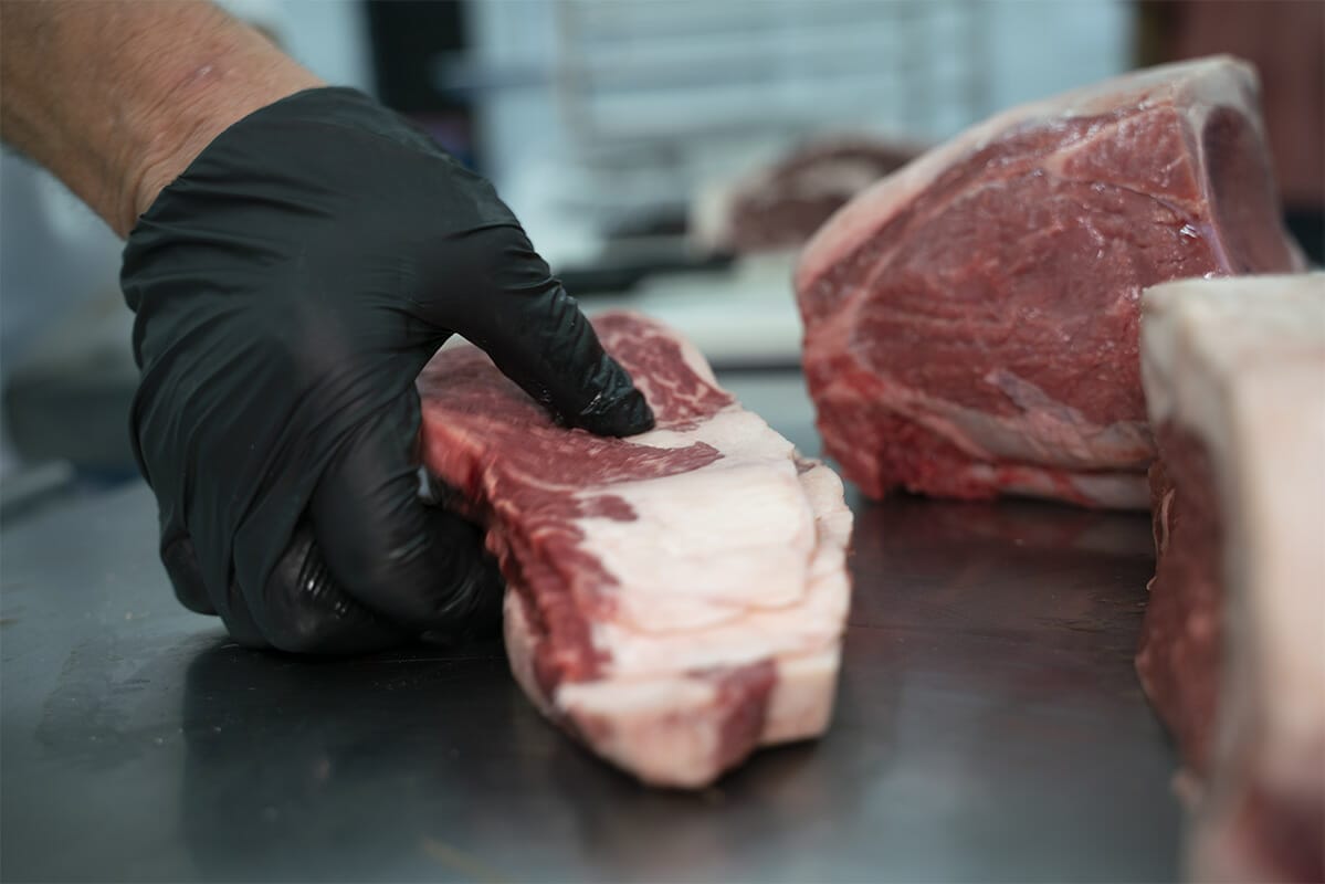 A butcher at 160 Processing is carefully placing a cut of meat on a butchers table.